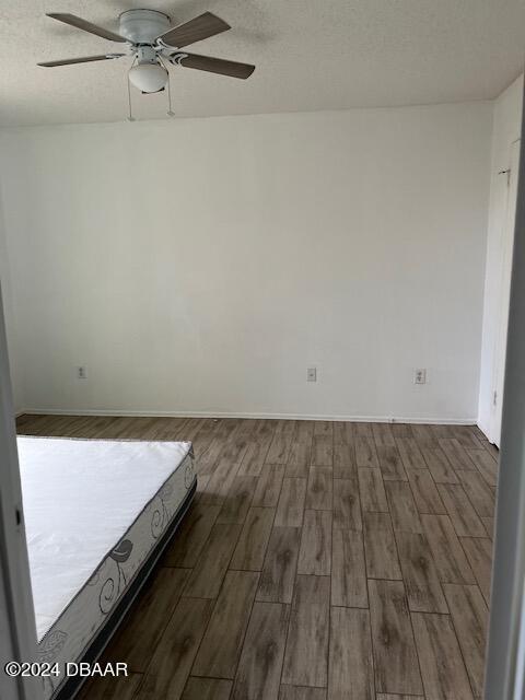 unfurnished bedroom with dark wood-type flooring, a textured ceiling, and ceiling fan