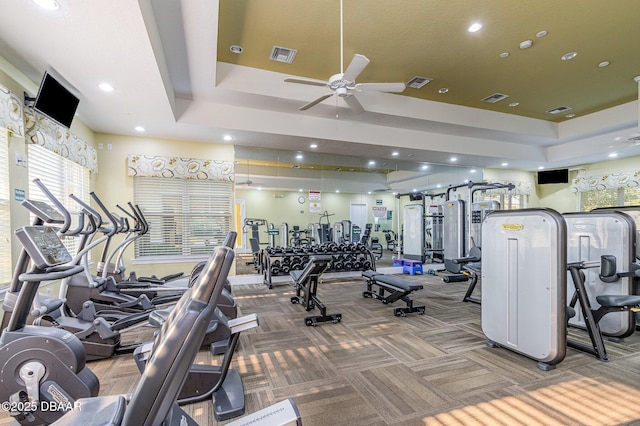 gym featuring a tray ceiling, carpet floors, and ceiling fan