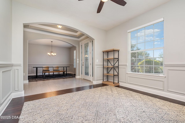 empty room with a raised ceiling, crown molding, ceiling fan with notable chandelier, and dark hardwood / wood-style flooring