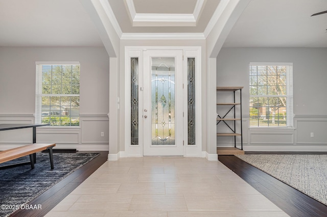 foyer with ornamental molding, a healthy amount of sunlight, a tray ceiling, and light hardwood / wood-style floors