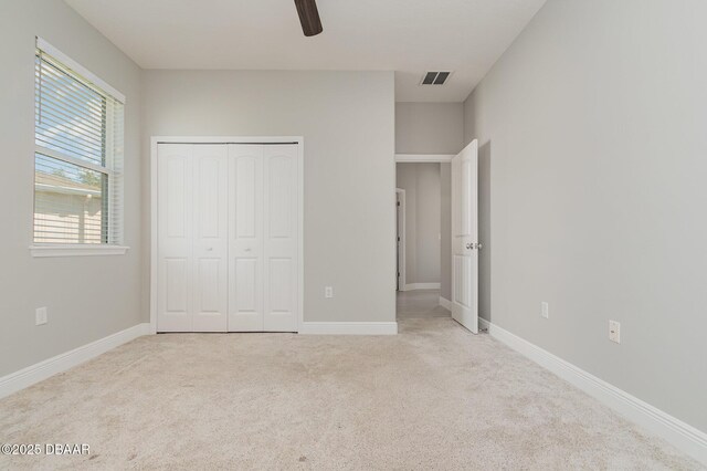 unfurnished bedroom featuring ceiling fan, light colored carpet, and a closet