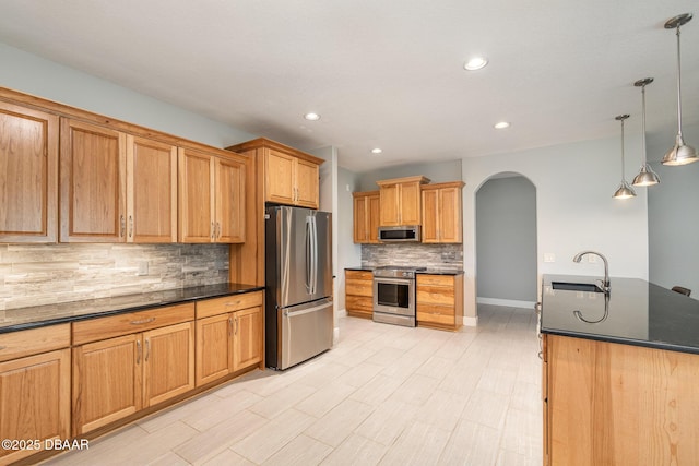 kitchen with pendant lighting, sink, stainless steel appliances, a center island with sink, and dark stone counters