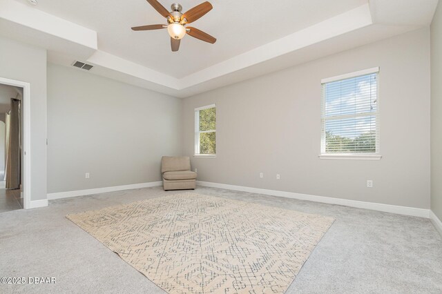 living area featuring light carpet, ceiling fan, and a tray ceiling