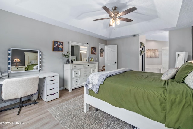 bedroom with visible vents, baseboards, a ceiling fan, a tray ceiling, and light wood finished floors