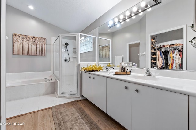 bathroom featuring a sink, wood finished floors, a shower stall, a bath, and double vanity