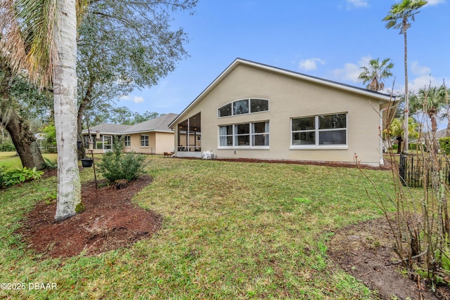 rear view of property with a sunroom, a lawn, fence, and stucco siding