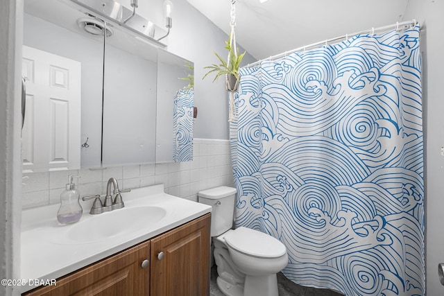 full bath featuring a shower with shower curtain, toilet, a wainscoted wall, vanity, and tile walls