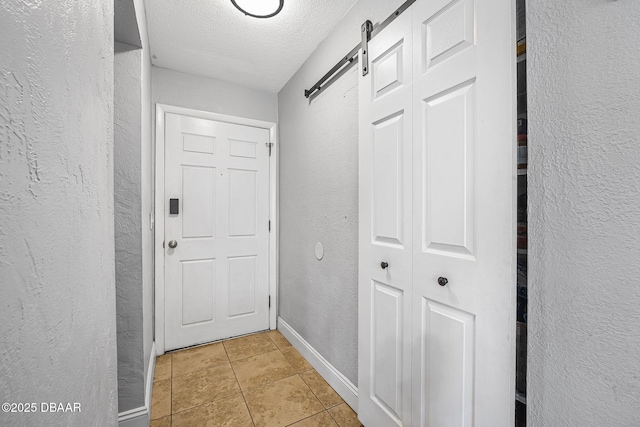 hall featuring a textured ceiling, a textured wall, a barn door, light tile patterned floors, and baseboards