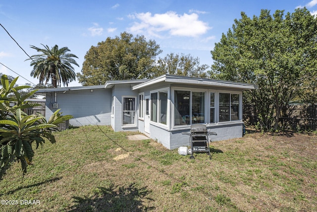 view of front of house featuring a front lawn, concrete block siding, fence, and a sunroom