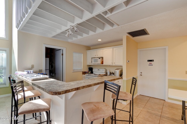 kitchen with a breakfast bar, white appliances, white cabinets, light tile patterned floors, and kitchen peninsula