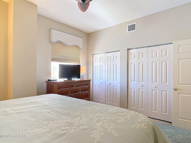 bedroom with a textured ceiling, visible vents, and two closets