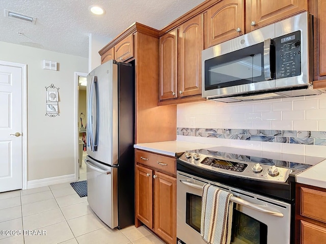 kitchen featuring brown cabinets, light tile patterned floors, visible vents, and stainless steel appliances