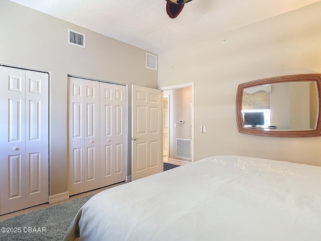 bedroom with a textured ceiling, visible vents, and two closets