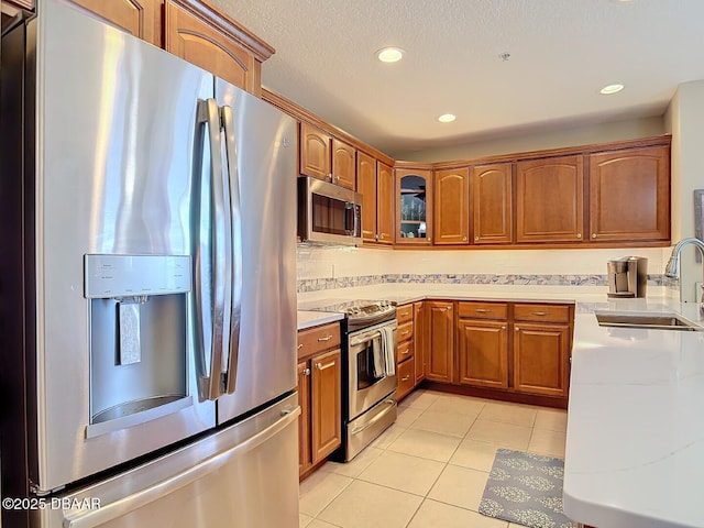 kitchen with light tile patterned floors, stainless steel appliances, light countertops, brown cabinetry, and a sink