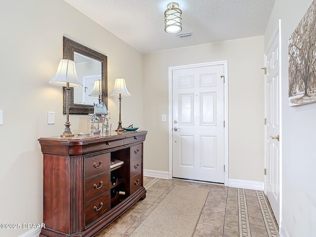 entryway featuring baseboards, visible vents, a textured ceiling, and light tile patterned flooring