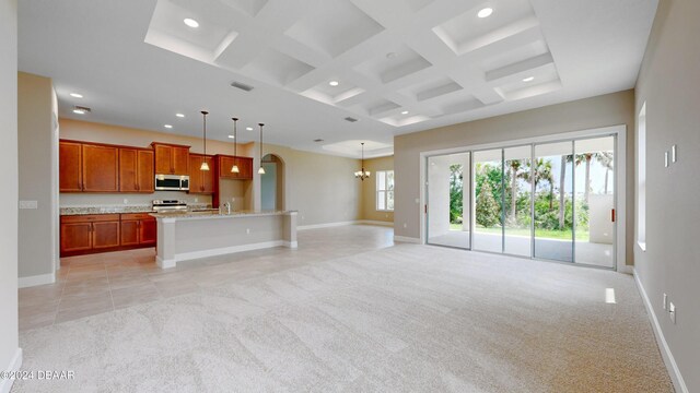 interior space featuring an inviting chandelier, light carpet, a kitchen island with sink, pendant lighting, and appliances with stainless steel finishes