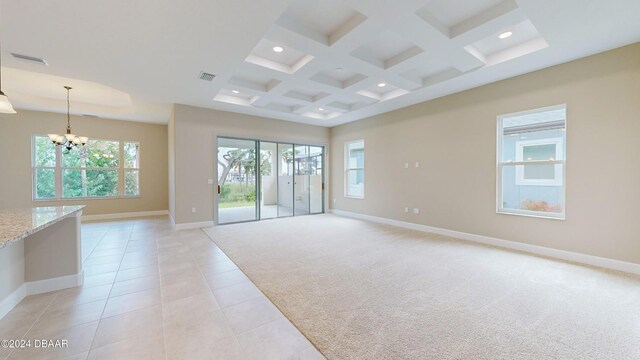 carpeted empty room with coffered ceiling, a notable chandelier, beam ceiling, and a healthy amount of sunlight