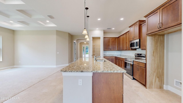 kitchen with sink, hanging light fixtures, stainless steel appliances, light stone counters, and a center island with sink