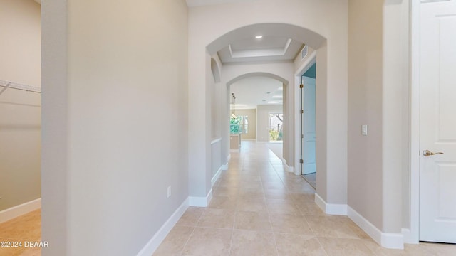 hall featuring light tile patterned flooring, a raised ceiling, and french doors