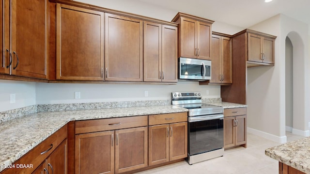 kitchen featuring stainless steel appliances, light tile patterned floors, and light stone counters