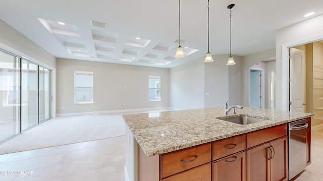 kitchen featuring sink, hanging light fixtures, coffered ceiling, light stone counters, and an island with sink