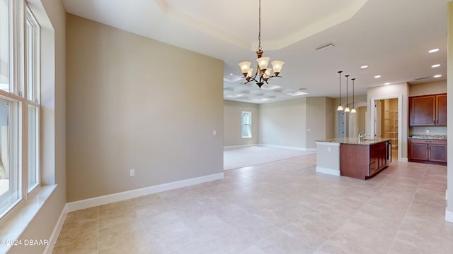 kitchen featuring decorative light fixtures, sink, light stone counters, a center island with sink, and an inviting chandelier