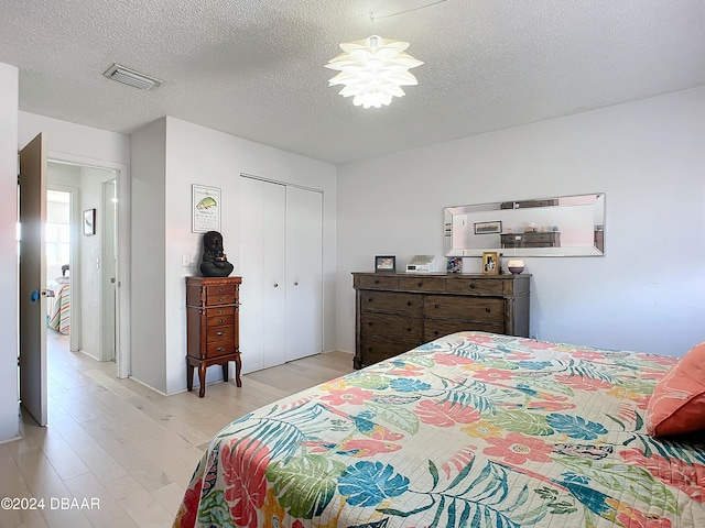 bedroom with light wood-type flooring, a textured ceiling, and a closet