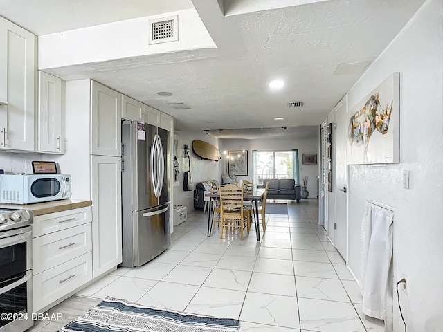 1510 Ocean Shore Blvd Unit 406, Ormond Beach, FL 32176 - kitchen with appliances with stainless steel finishes, white cabinets, light marble finish floors, open floor plan, and a textured ceiling