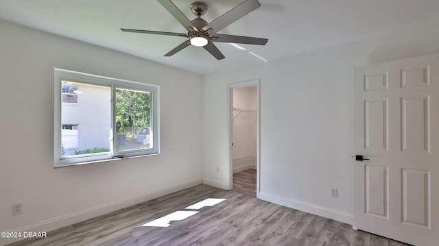 unfurnished bedroom with ceiling fan, a closet, a spacious closet, and light wood-type flooring