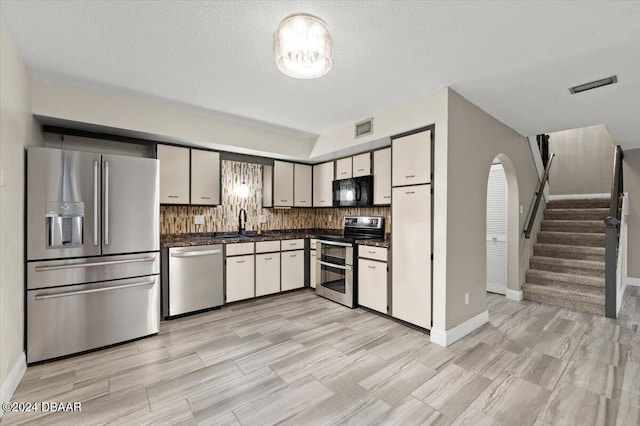 kitchen featuring tasteful backsplash, appliances with stainless steel finishes, a textured ceiling, sink, and light hardwood / wood-style floors