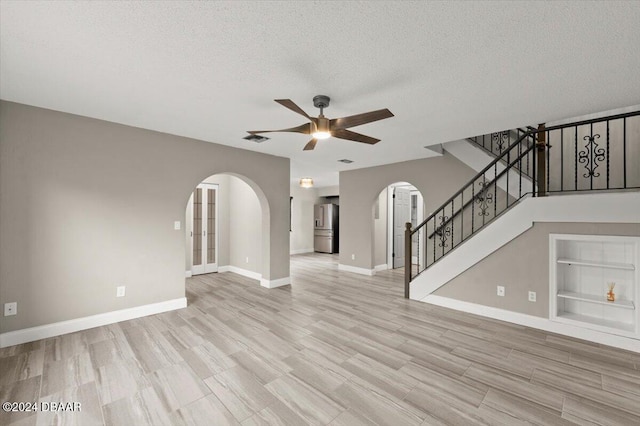 unfurnished living room featuring light wood-type flooring, built in features, a textured ceiling, and ceiling fan