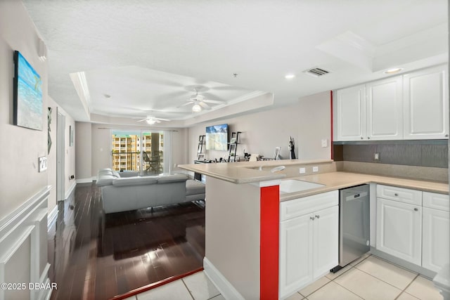 kitchen with kitchen peninsula, a raised ceiling, white cabinetry, and stainless steel dishwasher