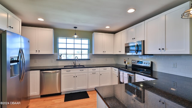 kitchen with stainless steel appliances, sink, pendant lighting, light hardwood / wood-style flooring, and white cabinets