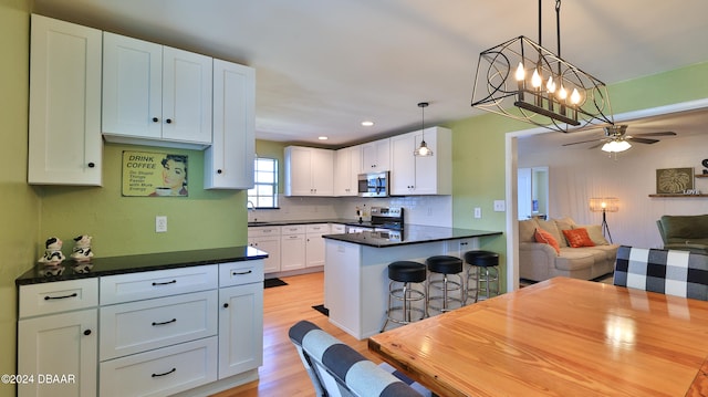 kitchen with pendant lighting, white cabinets, ceiling fan with notable chandelier, a kitchen bar, and stainless steel appliances