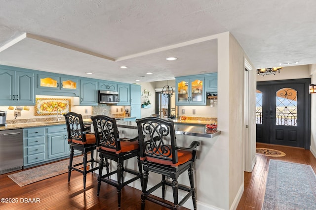 761 Marina Point Dr Unit 7610, Daytona Beach, FL 32114 - kitchen with glass insert cabinets, dark wood-style floors, blue cabinetry, a kitchen bar, and appliances with stainless steel finishes