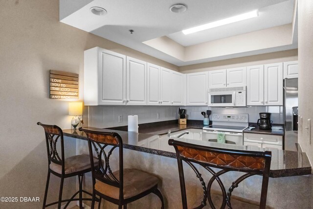 5300 S Atlantic Ave Unit 16-505, New Smyrna Beach, FL 32169 - kitchen with a peninsula, white appliances, a breakfast bar, white cabinetry, and decorative backsplash