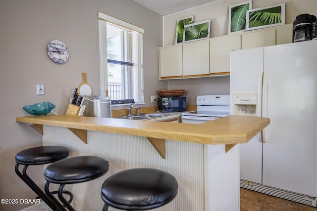 3370 Ocean Shore Blvd Unit 202B, Ormond Beach, FL 32176 - kitchen with white appliances, a breakfast bar area, dark tile patterned floors, white cabinets, and a textured ceiling