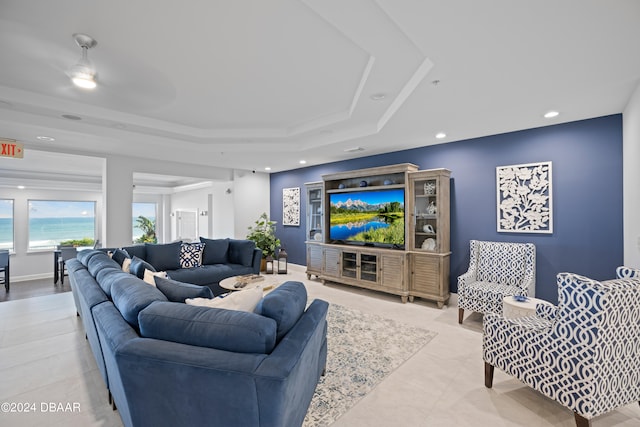 living room with ceiling fan, a raised ceiling, and a water view