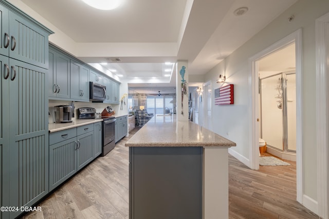 kitchen with stainless steel appliances, light stone counters, a raised ceiling, light hardwood / wood-style flooring, and a kitchen island