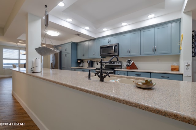 kitchen with blue cabinetry, dark hardwood / wood-style floors, light stone counters, and appliances with stainless steel finishes