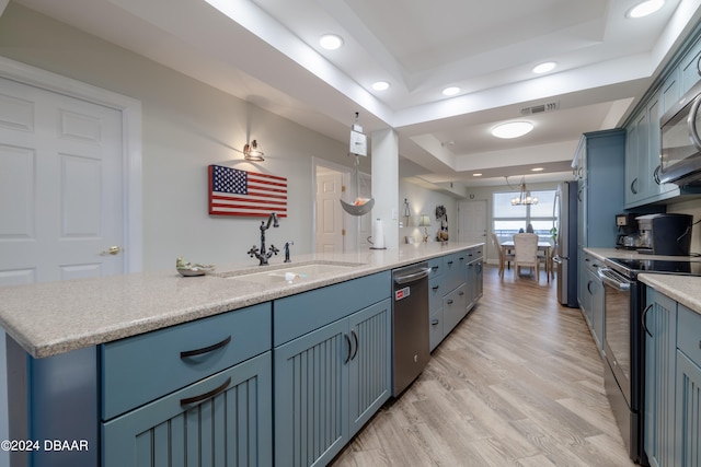 kitchen featuring blue cabinets, a tray ceiling, pendant lighting, light wood-type flooring, and appliances with stainless steel finishes