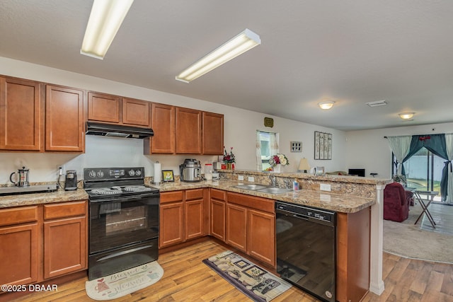 kitchen with kitchen peninsula, light hardwood / wood-style flooring, sink, light stone counters, and black appliances