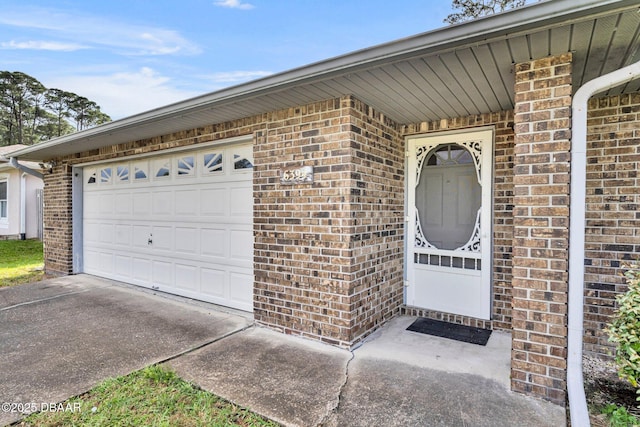 view of exterior entry featuring brick siding, a garage, and driveway