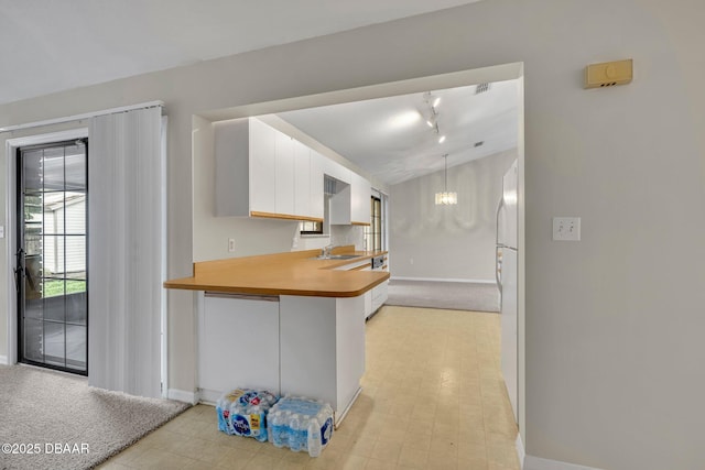 kitchen featuring baseboards, lofted ceiling, a notable chandelier, white cabinetry, and a sink