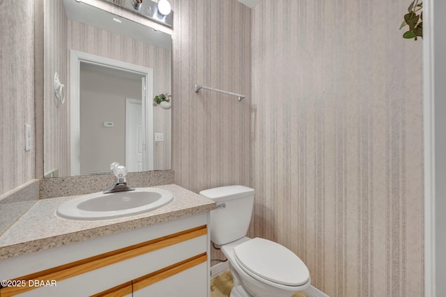 bathroom featuring toilet, wallpapered walls, and vanity