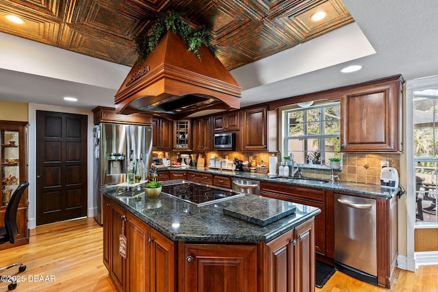 kitchen featuring sink, light wood-type flooring, a kitchen island, custom exhaust hood, and appliances with stainless steel finishes