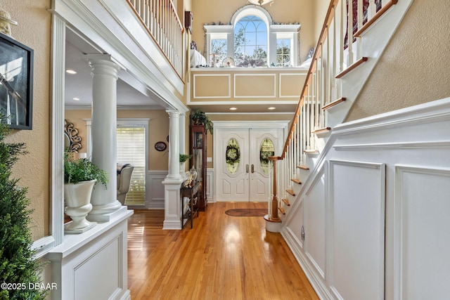 foyer with french doors, light hardwood / wood-style flooring, a towering ceiling, ornamental molding, and decorative columns