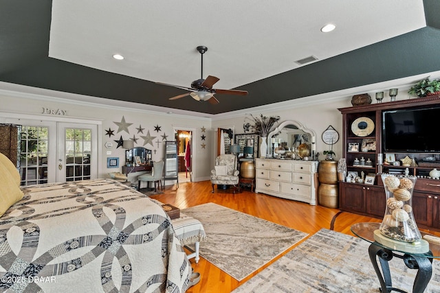 bedroom featuring french doors, light wood-type flooring, a tray ceiling, and ceiling fan