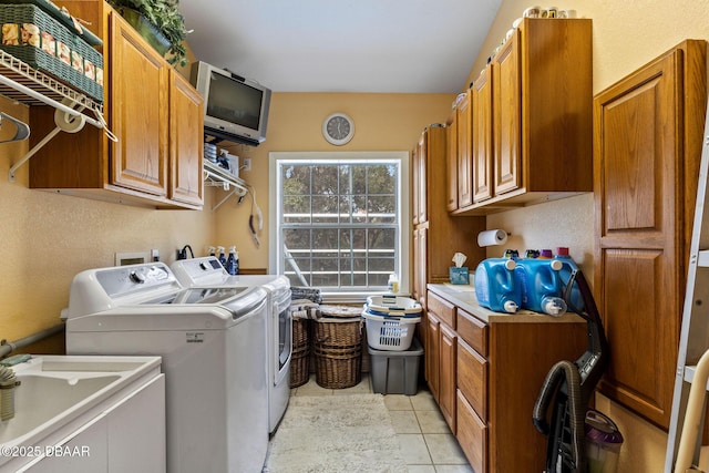 clothes washing area with cabinets, light tile patterned floors, washer and clothes dryer, and sink