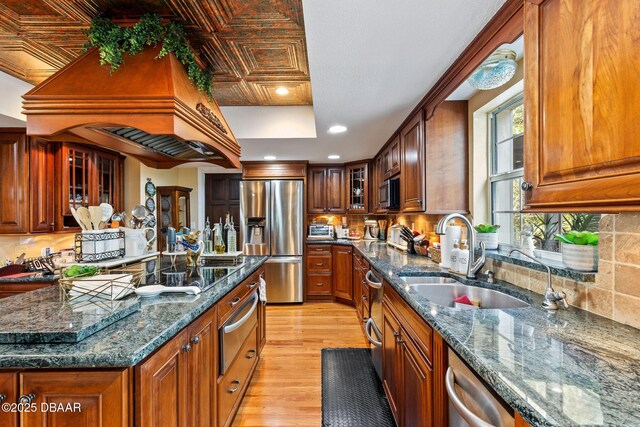 kitchen with premium range hood, sink, light hardwood / wood-style flooring, dark stone countertops, and stainless steel appliances